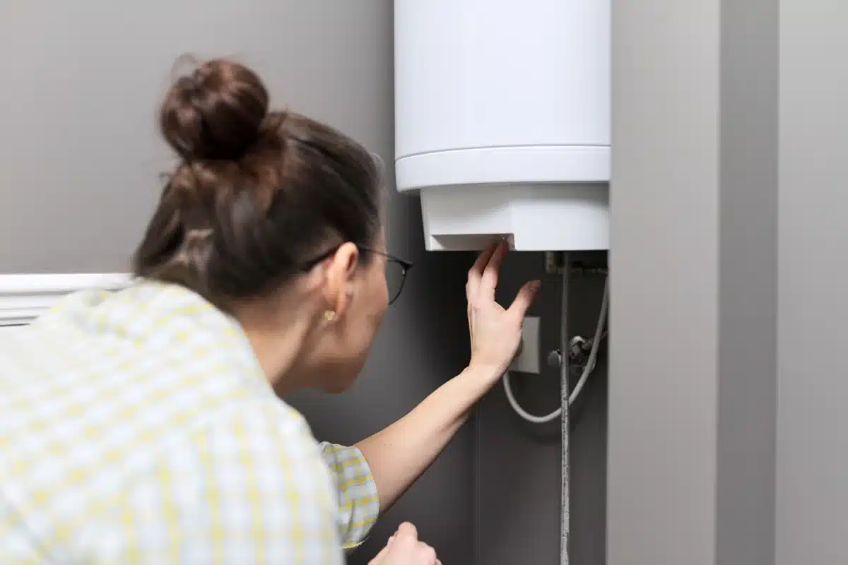 A homeowner inspecting a wall-mounted storage water heater, checking the unit’s connections and built-in safety features